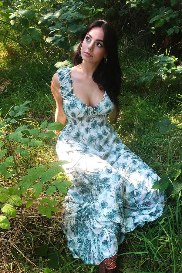 Model wears Maisie Maxi Dress in Lily pad Green Watercolour Floral, a retro floaty frill dress inspired by the 70s bohemian fashion by All About Audrey