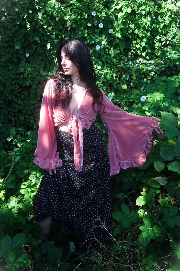 model image of our Velvet Venus Wrap Top in Dusty Pink. A romantic earthy rouge hue in a soft shimmering velvet. Featuring huge bell sleeves with a frill edge. Shown here tied at the front inspired by 70's bohemia styles. By All About Audrey