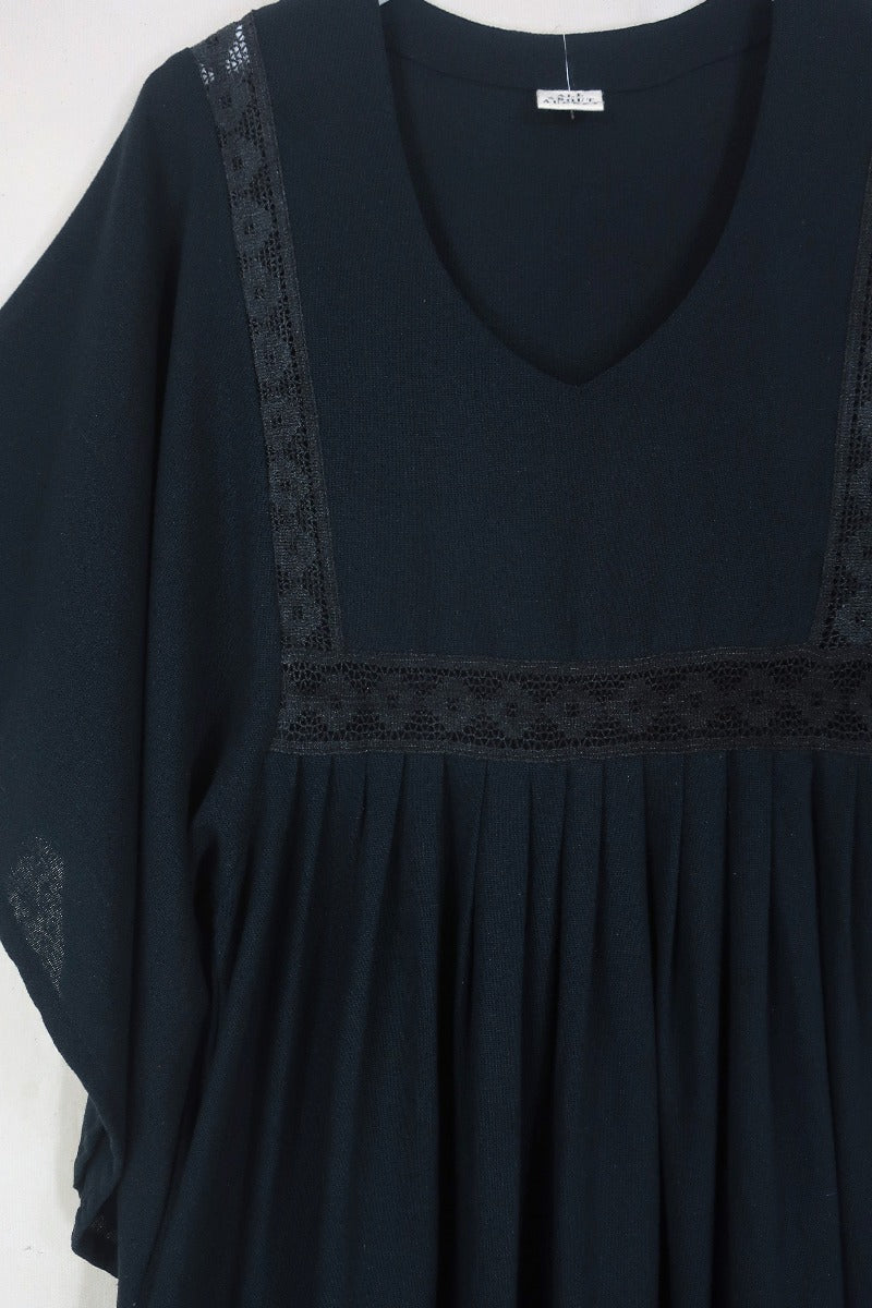 Close up flat lay of our Cordelia Midi Dress in Nightshade Black. Showing off the full skirt, tapered sleeves and crochet detailing inspired by 1970s folk designs. By All About Audrey