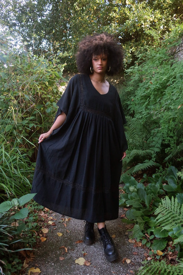 Model wears our Cordelia Midi Dress in Nightshade Black as an oversized loose smock style fit. She shows off the full skirt, tapered sleeves and crochet detailing inspired by 1970s folk designs. By All About Audrey 