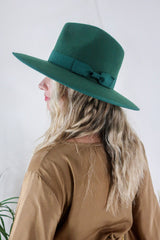 Model wears our Sierra hat in Forest Green. A natural jewelled earthy green inspired by vintage 1970s prairie and western cowboy styles. Classic wide brim and high crown Fedora design with a decorative ribbon and trim by All About Audrey