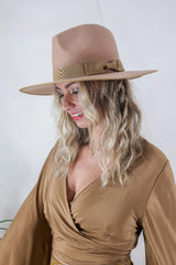 Model wears our Sierra hat in Tan. A natural warm earthy beige inspired by vintage 1970s prairie and western cowboy styles. Classic wide brim and high crown Fedora design with a decorative ribbon and trim by All About Audrey