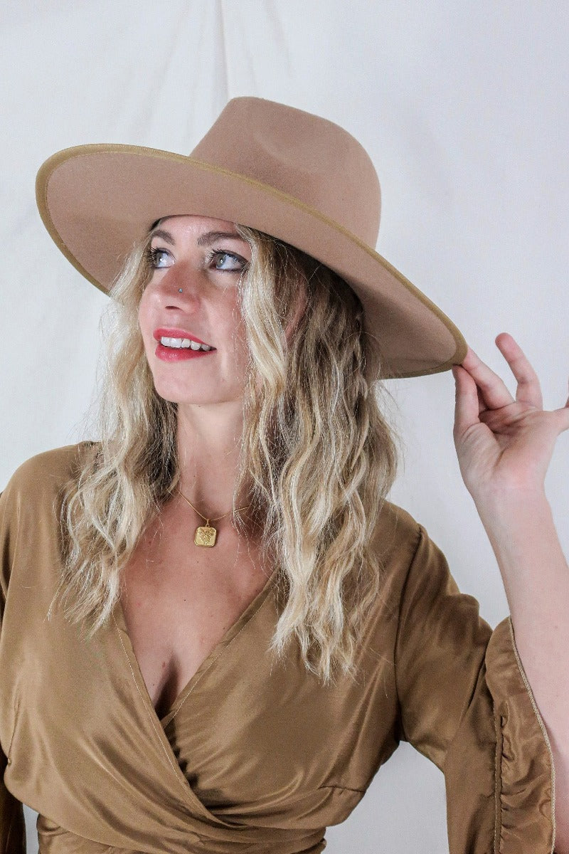 Model wears our Sierra hat in Tan. A natural warm earthy beige inspired by vintage 1970s prairie and western cowboy styles. Classic wide brim and high crown Fedora design with a decorative ribbon and trim by All About Audrey