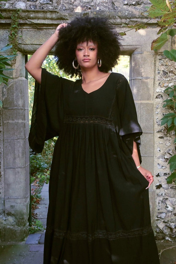 Close up of our model who wears our Cordelia Midi Dress in Nightshade Black as an oversized loose smock style fit. She shows off the full skirt, tapered sleeves and crochet detailing inspired by 1970s folk designs. By All About Audrey
