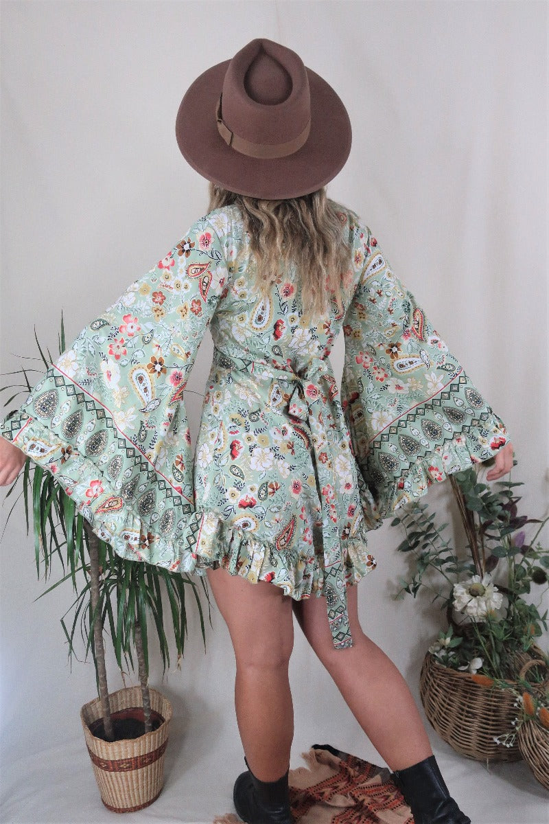 Model wears our Venus Mini Frill Wrap dress in Porcelain Green. A beautiful ornate print reminiscent of bohemian flora from the 70s in a soft sage tone with golds and pinks. By All About Audrey