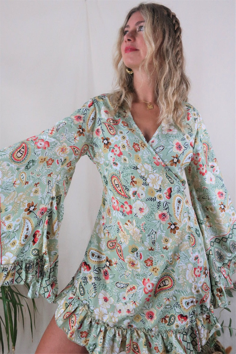 Model wears our Venus Mini Frill Wrap dress in Porcelain Green. A beautiful ornate print reminiscent of bohemian flora from the 70s in a soft sage tone with golds and pinks. By All About Audrey