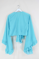 Flat lay of our Velvet Venus Wrap Top in Sky Blue. A retro bold aqua blue hue in a soft shimmering velvet. Featuring huge bell sleeves with a frill edge. Shown tied at the front inspired by 70's bohemia styles. By All About Audrey