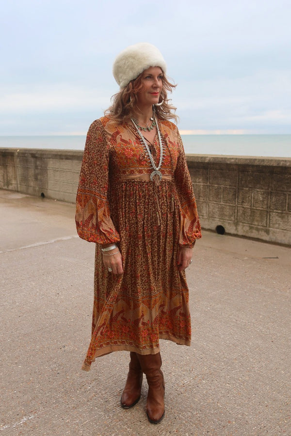 Audrey wears our Peacock Primrose Dress in Tan & Tumeric. An earthy golden tone with a vintage inspired 1970s peacock, floral print. Worn loose and flowing and paired with chunky boho silver jewellery and our Anastasia hat in Cream. By All About Audrey