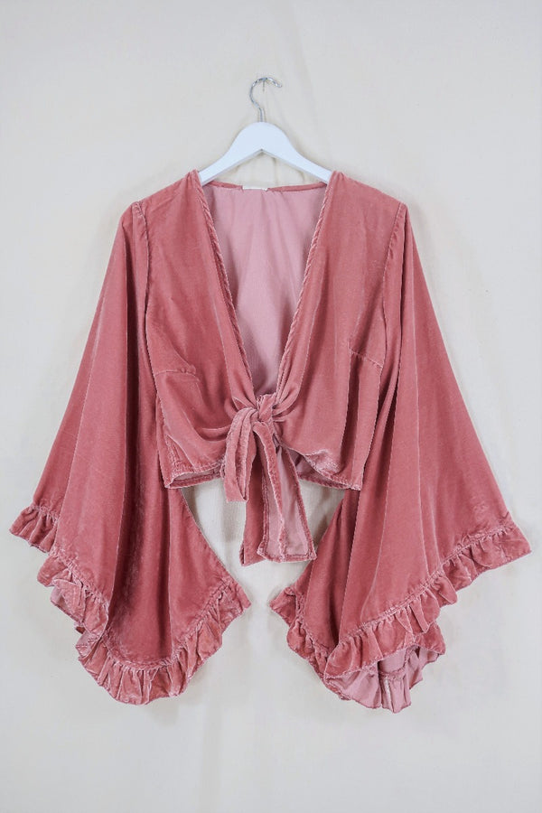 Flat lay of our Velvet Venus Wrap Top in Dusty Pink. A romantic earthy rouge hue in a soft shimmering velvet. Featuring huge bell sleeves with a frill edge. Shown here tied at the front inspired by 70's bohemia styles. By All About Audrey