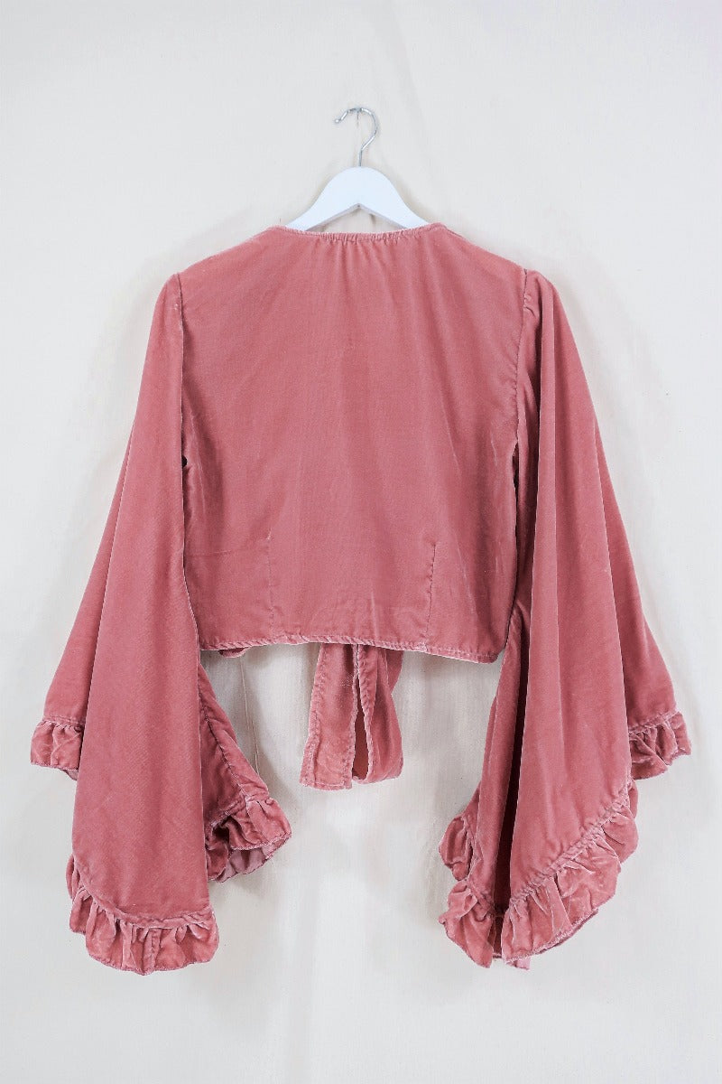 Flat lay of our Velvet Venus Wrap Top in Dusty Pink. A romantic earthy rouge hue in a soft shimmering velvet. Featuring huge bell sleeves with a frill edge. Shown here tied at the front inspired by 70's bohemia styles. By All About Audrey