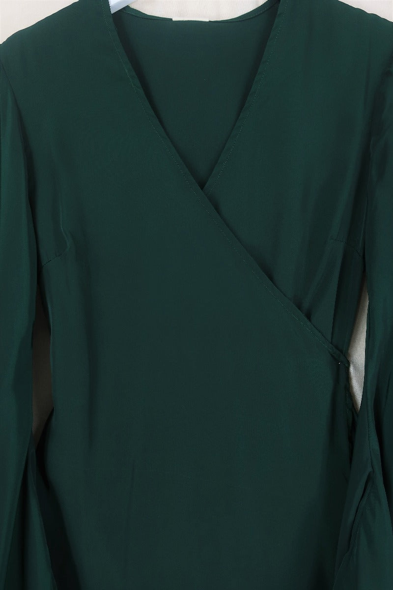 Flat lay of our Venus Khroma wrap dress in Archer Green, a darker jewel green tone which is easy to style and versatile to wear! Inspired by 70's bohemia by All About Audrey
