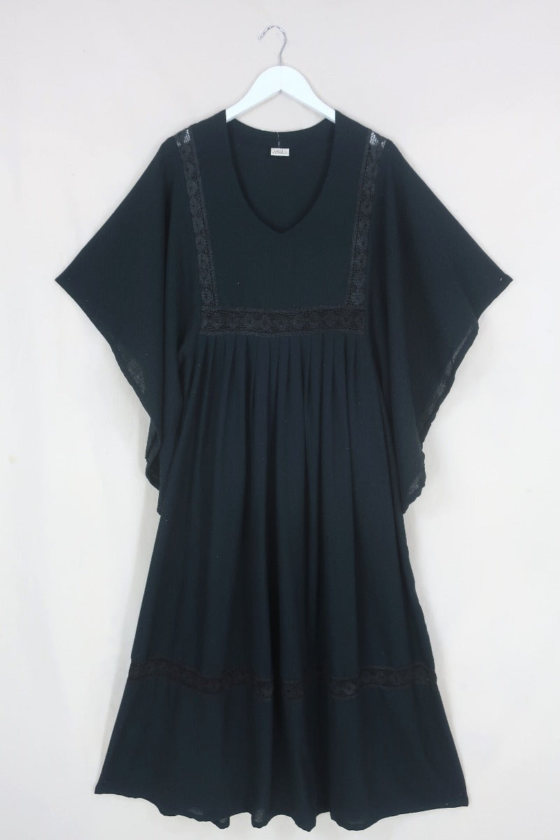 Front flat lay of our Cordelia Midi Dress in Nightshade Black. Showing off the full skirt, tapered sleeves and crochet detailing inspired by 1970s folk designs. By All About Audrey