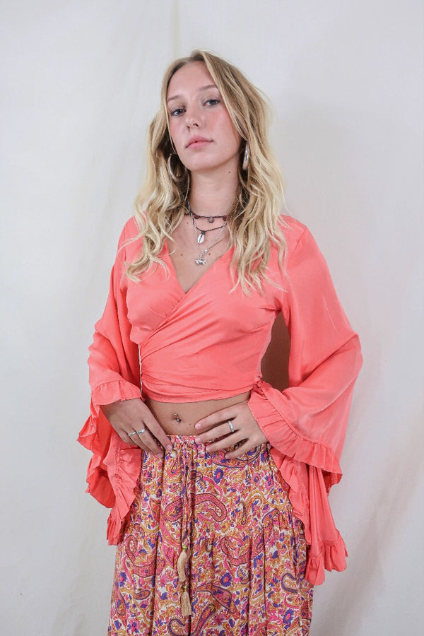 Model wears our Khroma Venus wrap top in a vibrant Miami Peach colour. Worn as a wraparound style with long floaty butterfly frill sleeves by All About Audrey