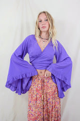 Photo shows model wearing electric lilac Khroma Venus top with frilled 70s inspired bell sleeves and a wrap style front by All About Audrey