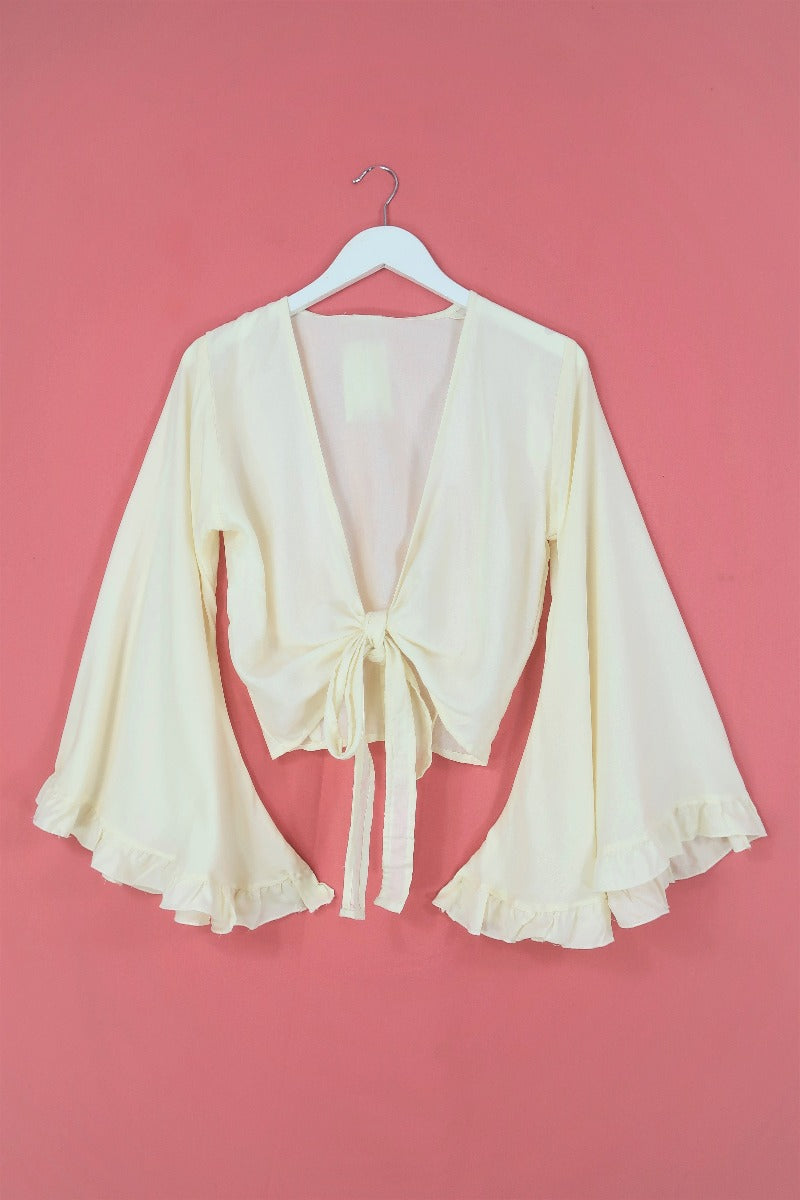 Flat lay shot of our beautiful boho bell sleeve wrap top with 70's inspired frill trim in a elegant cream coconut white by All About Audrey