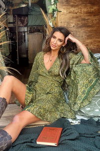 Model wears our Venus Mini Wrap Dress in Coltrane Green Mandala. A vibrant psychedelic mosaic print of warm retro greens by All About Audrey