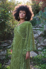 Model wears our Khroma Venus Maxi Dress in Elven Green Velvet. Worn like a wrap style and tied at the back with huge floaty retro inspired bell sleeves. By All About Audrey