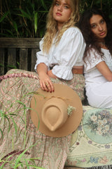 Model holds our Sierra hat in Fawn. A light natural beige inspired by vintage 1970s prairie and western cowboy styles. Classic wide brim and high crown Fedora design with a decorative thin ribbon and simple brim by All About Audrey