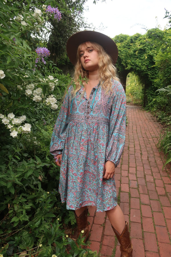 Model wears our Florence mini dress in Powder Blue & Peach Paisley Floral. With an above knee length skirt, balloon sleeves and a button up front inspired by the 1970s bohemian style. By All About Audrey