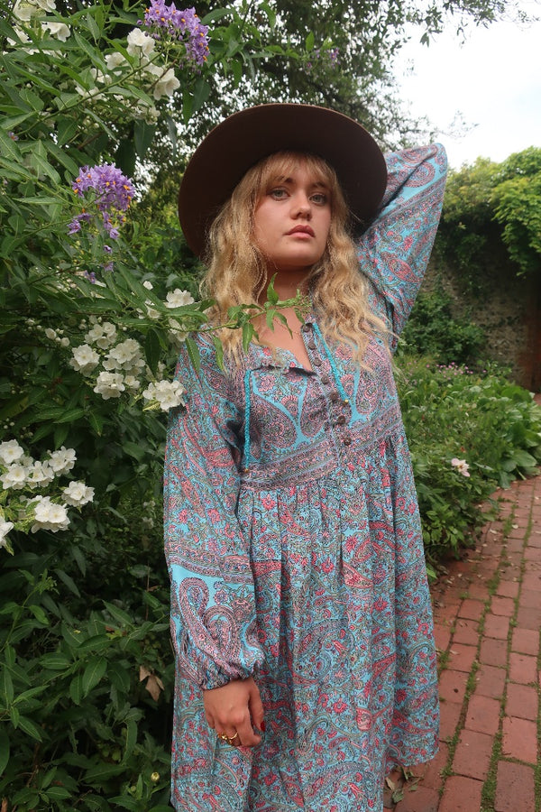 Model wears our Florence mini dress in Powder Blue & Peach Paisley Floral. With an above knee length skirt, balloon sleeves and a button up front inspired by the 1970s bohemian style. By All About Audrey