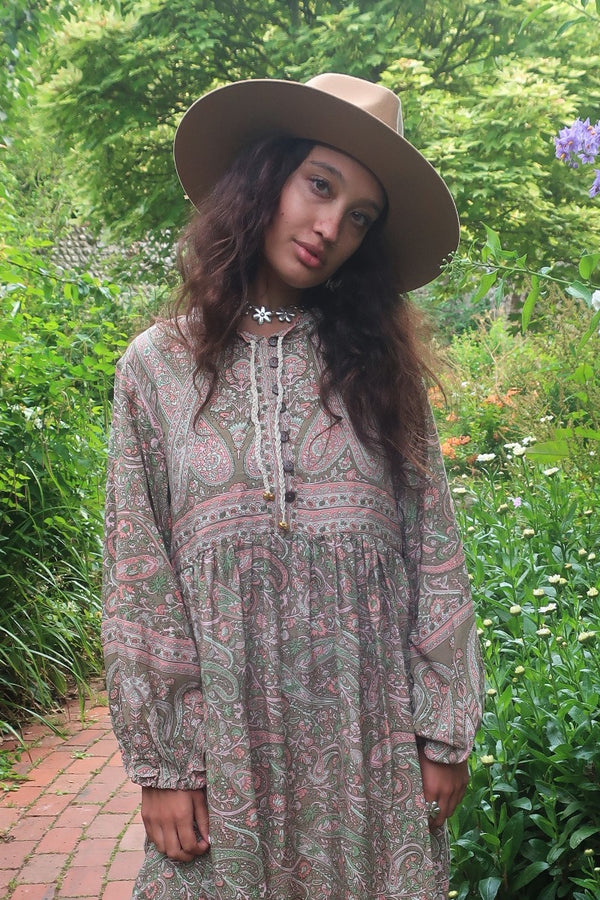 Model wears our Florence Mini Dress in Sage & Blush Paisley Floral. With a knee length skirt, button up front and retro balloon sleeves inspired by 1970s bohemian style by All About Audrey