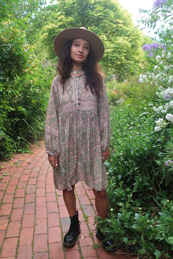 Model wears our Florence Mini Dress in Sage & Blush Paisley Floral. With a knee length skirt, button up front and retro balloon sleeves inspired by 1970s bohemian style by All About Audrey