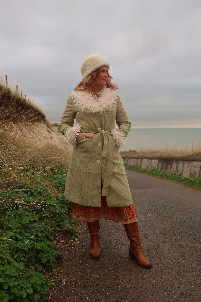 Audrey wears our Janis Long Coat in Agate Green Corduroy. Worn tied at the front showing off the belt and pockets. A classic retro 70's style and colour-way.