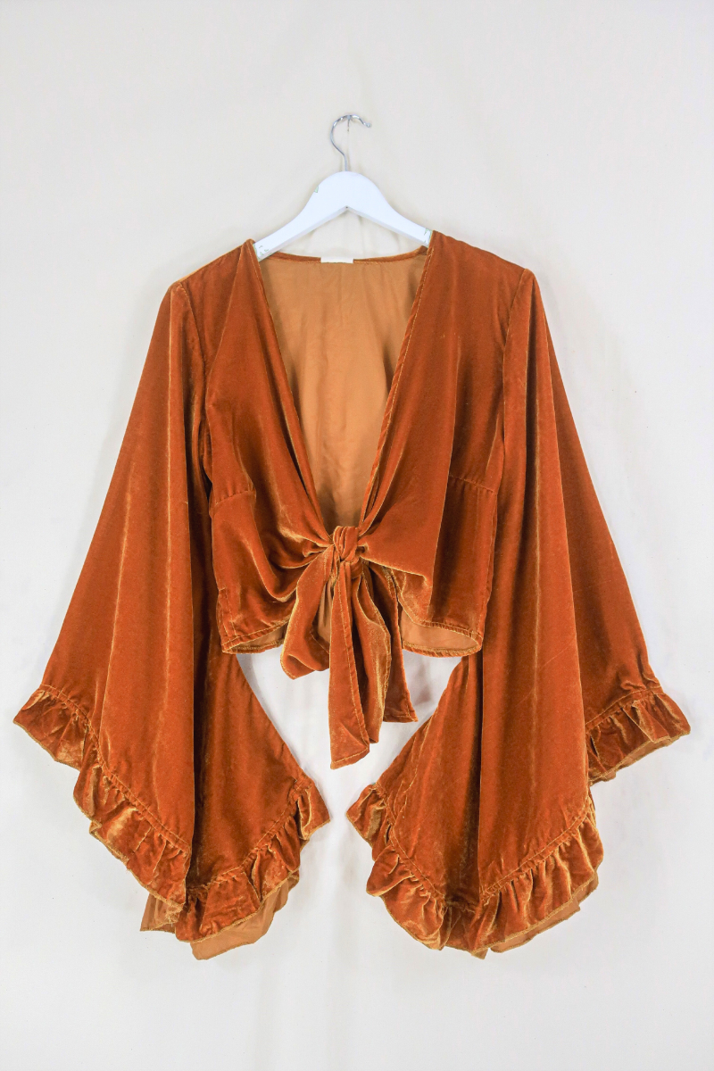 Flat lay of our Velvet Venus Wrap Top in Marmalade Yellow. A dark, warm honey mustard hue in a soft shimmering velvet. Featuring huge bell sleeves with a frill edge. Here it is tied at the front as a tie top inspired by 70's bohemia styles. By All About Audrey