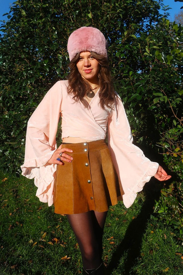 model styling one of our Velvet Venus Wrap Top in Powder Pink. An ethereal petal pink hue in a soft shimmering velvet. Featuring huge bell sleeves with a frill edge. Shown here tied at the front inspired by 70's bohemia styles. By All About Audrey