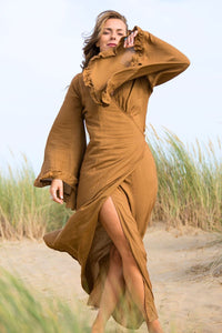 Model wears our bohemian bell sleeve wrap maxi dress in cinnamon brown. Long floaty sleeves with a ruffle hem and a wraparound tie waist to create an elegant shape by all about audrey