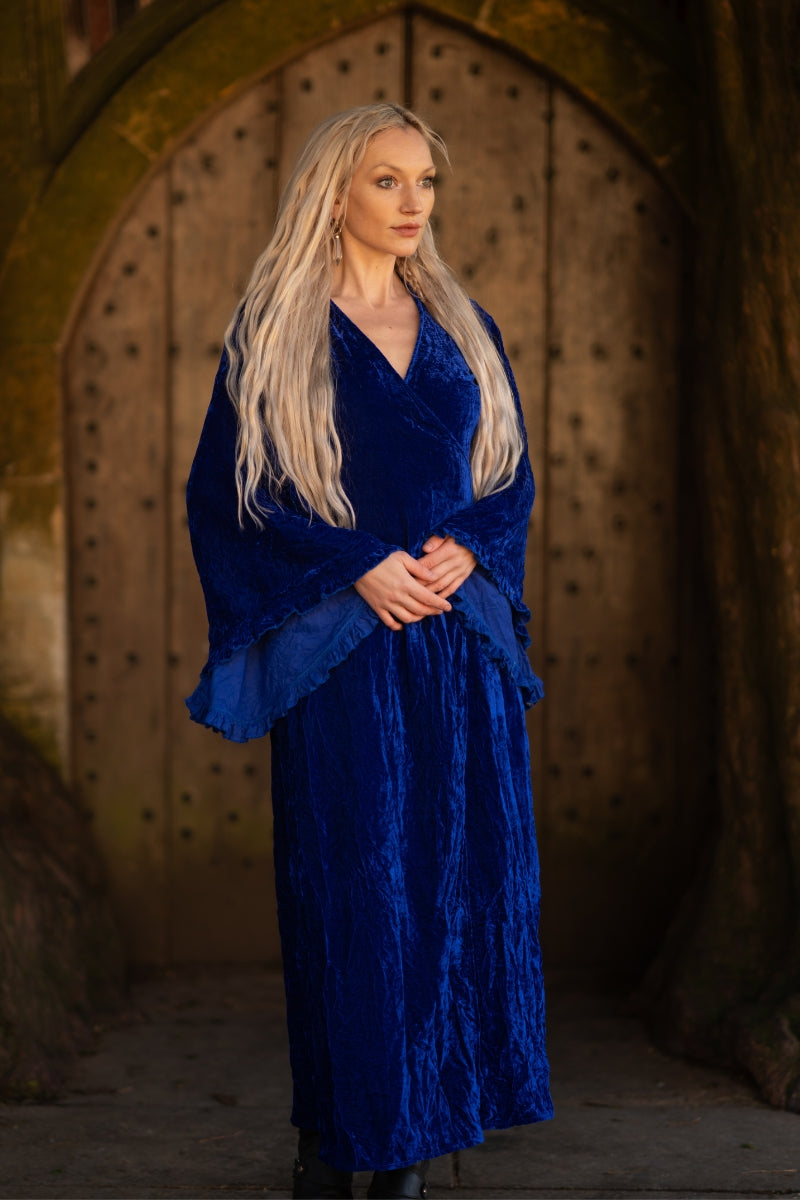 Model wears our Khroma Venus Maxi Dress in Regal Blue Velvet. Showing off the vintage 1970s inspired bell sleeves and worn in a wrap style, tied at the back. By All About Audrey