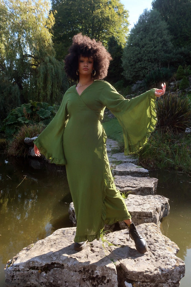 Model wears our Khroma Venus Robe Dress in Pixie Green as a wrap style dress, showing off the huge bell sleeves and frill trim on the sleeves and front. All About Audrey