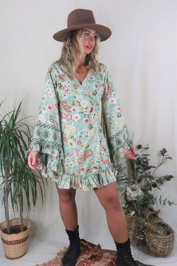 Model wears our Venus Mini Frill Wrap dress in Porcelain Green. A beautiful ornate print reminiscent of bohemian flora from the 70s in a soft sage tone with golds and pinks. By All About Audrey