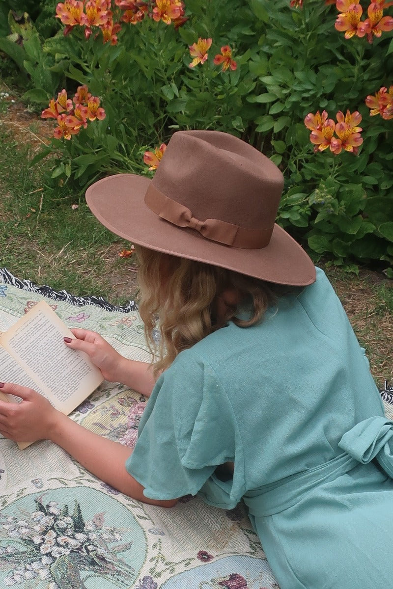 Model wears our Sierra hat in Saddle Brown. A natural cool earthy brown inspired by vintage 1970s prairie and western cowboy styles. Classic wide brim and high crown Fedora design with a decorative ribbon and trim by All About Audrey