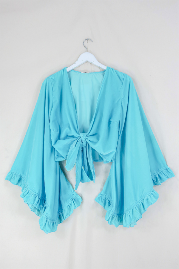 Flat lay of our Velvet Venus Wrap Top in Sky Blue. A retro bold aqua blue hue in a soft shimmering velvet. Featuring huge bell sleeves with a frill edge. Shown tied at the front inspired by 70's bohemia styles. By All About Audrey