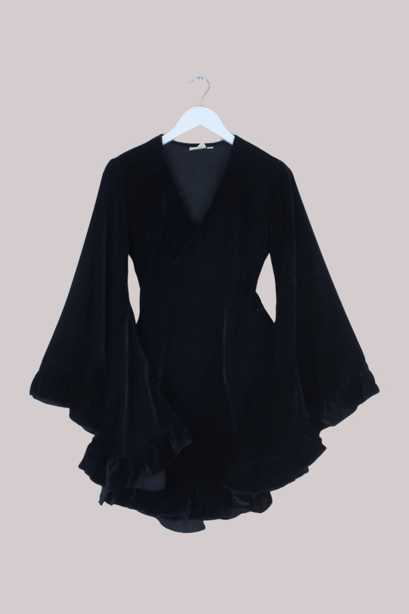 Black velvet dress on a hanger against a beige background