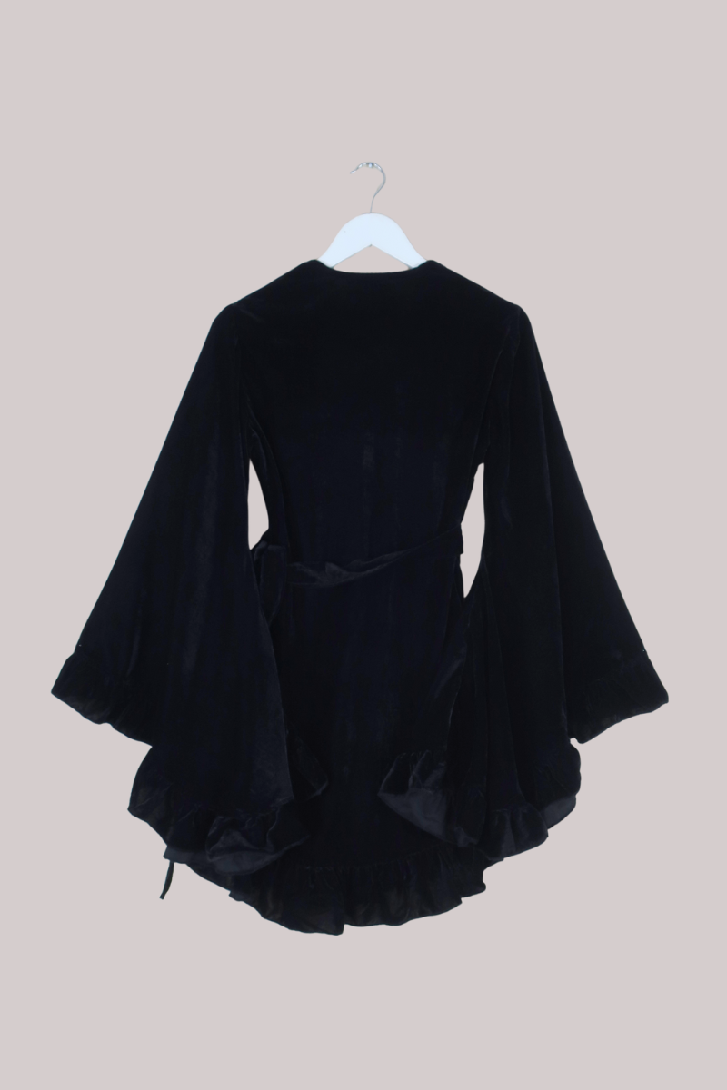 Black velvet dress on a hanger against a beige background
