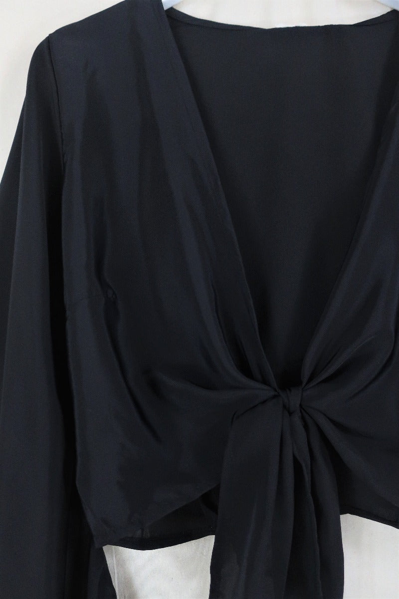 Flat lay of our Venus Khroma wrap top in Vampy Black. Classic black tone that's easy to style. Inspired by 70's bohemia by All About Audrey