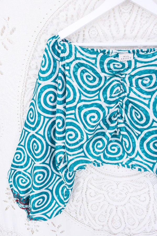 Front view, close up of this groovy Ariel top . Covered in psychedelic swirls in tones of icy white and teal. Chilli red detailing on the cuffs.  