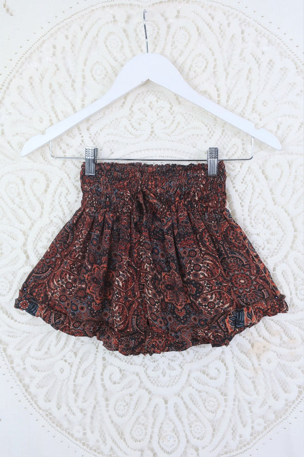 Front view of our Venus frilly shorts in rust and jet mandala.  The print is a mandala tile print with black, rust with stone blue details.  The waist band is ruched with a tie belt. These shorts are free size. 
