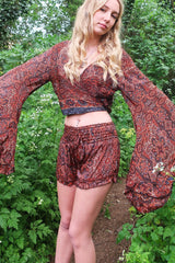 Photo shows model wearing our Venus frilly shorts in rust and jet mandala. The print is a mandala tile print with black, rust with stone blue details. The waist band is ruched with a tie belt. These shorts are free size.