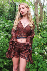 Photo shows model wearing our Venus frilly shorts in rust and jet mandala. The print is a mandala tile print with black, rust with stone blue details. The waist band is ruched with a tie belt. These shorts are free size.