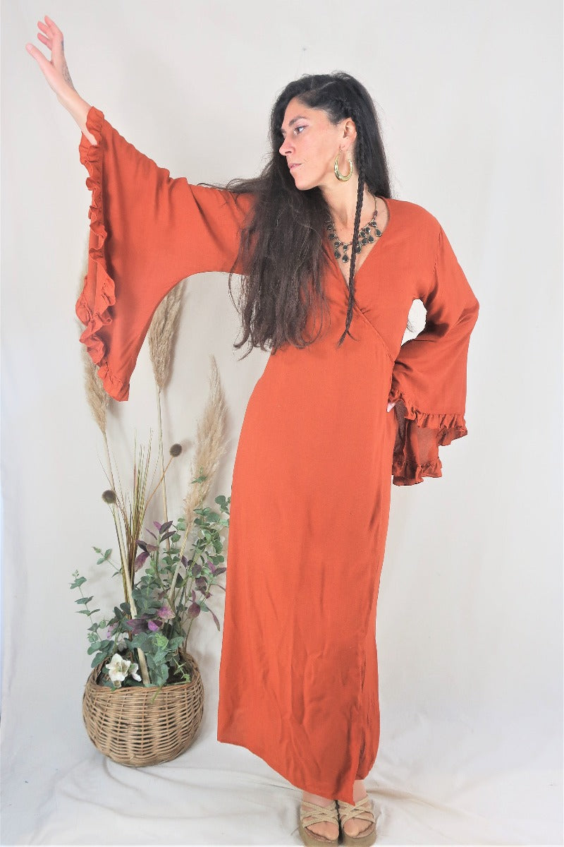 Model wears our Venus dress in red clay. Showing off the long floaty ruffle bell sleeves and wrap tie waist. A beautifully soft rayon fabric by All About Audrey
