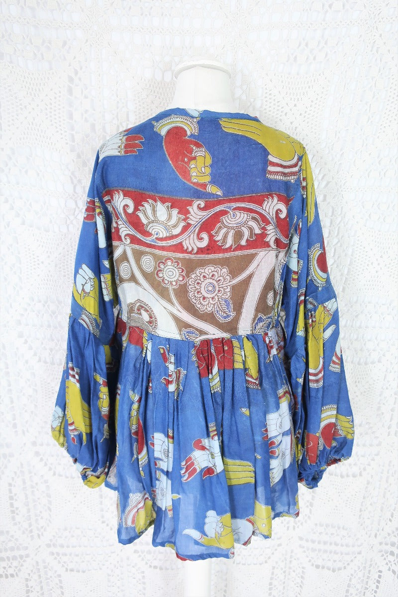 Photo shows back of a deep blue peacock and hand gesture block printed boho smock top with a tie neck and balloon sleeves.