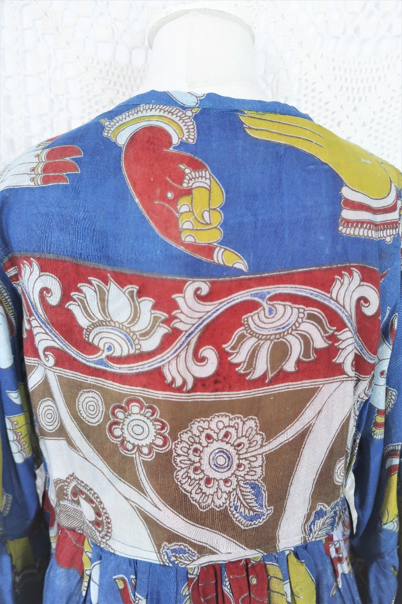 Photo shows close up back of a deep blue peacock and hand gesture block printed boho smock top with a tie neck and balloon sleeves.