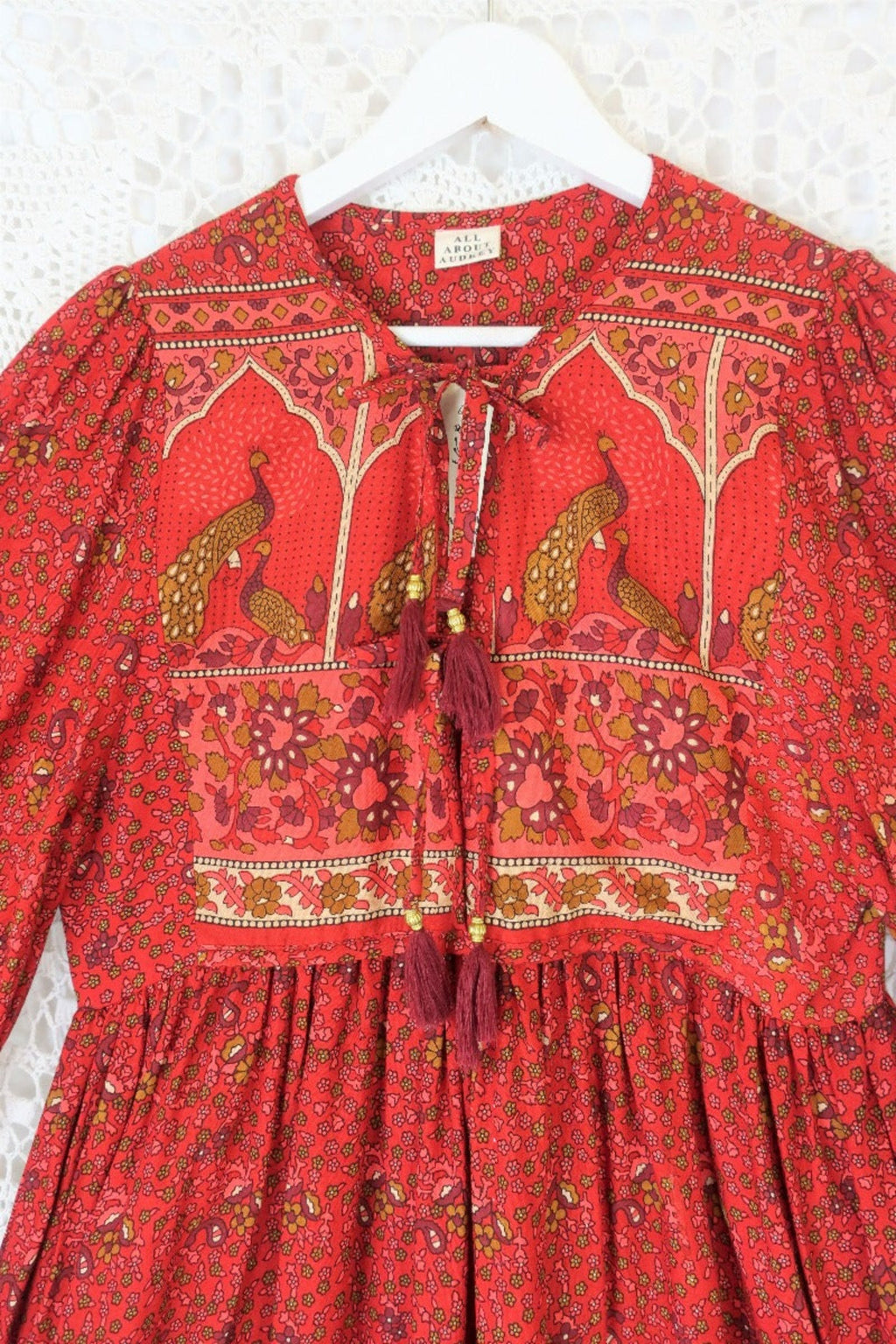 detail of contrast printed double tassel tie yolk on balloon sleeve smocked style peacock primrose midi dress in berry red with gold detailed vintage inspired indian peacock design from our collection of bohemian dresses by all about audrey