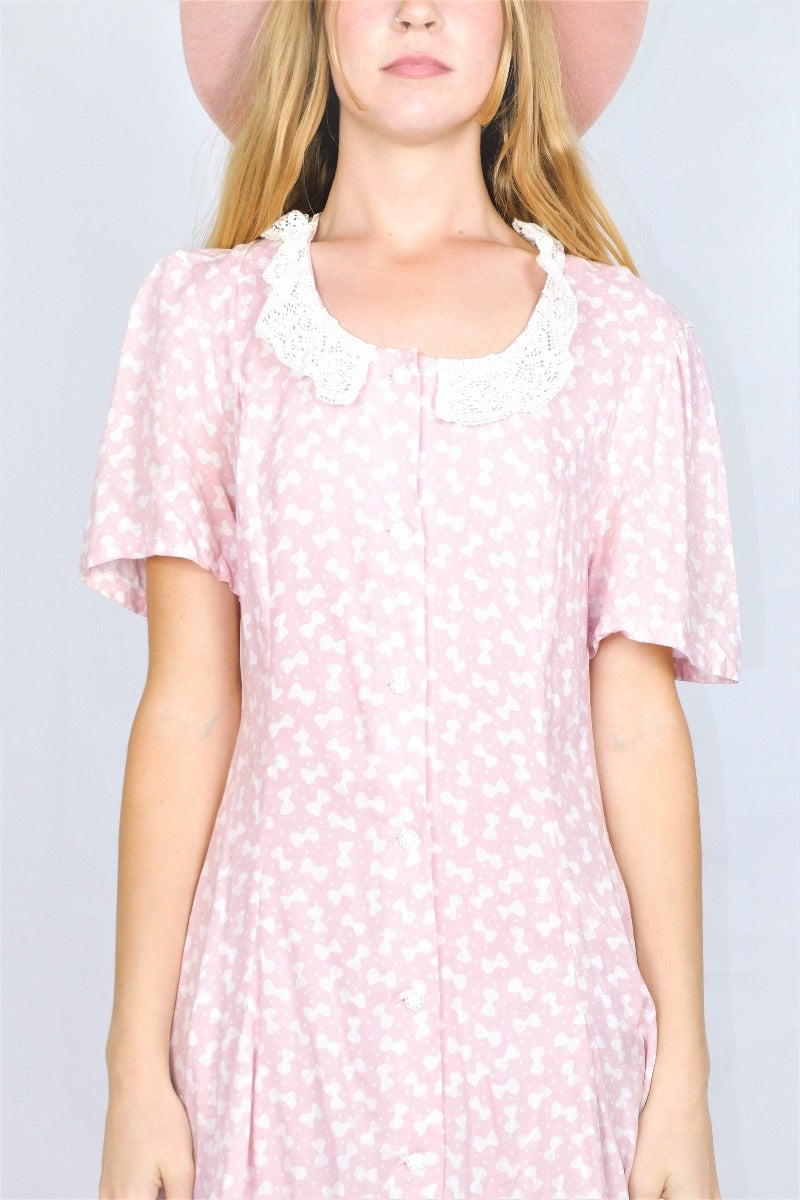 Close up Photo of print and detailing on baby pink bowtie polka dot printed mini shift dress with a lace collar.