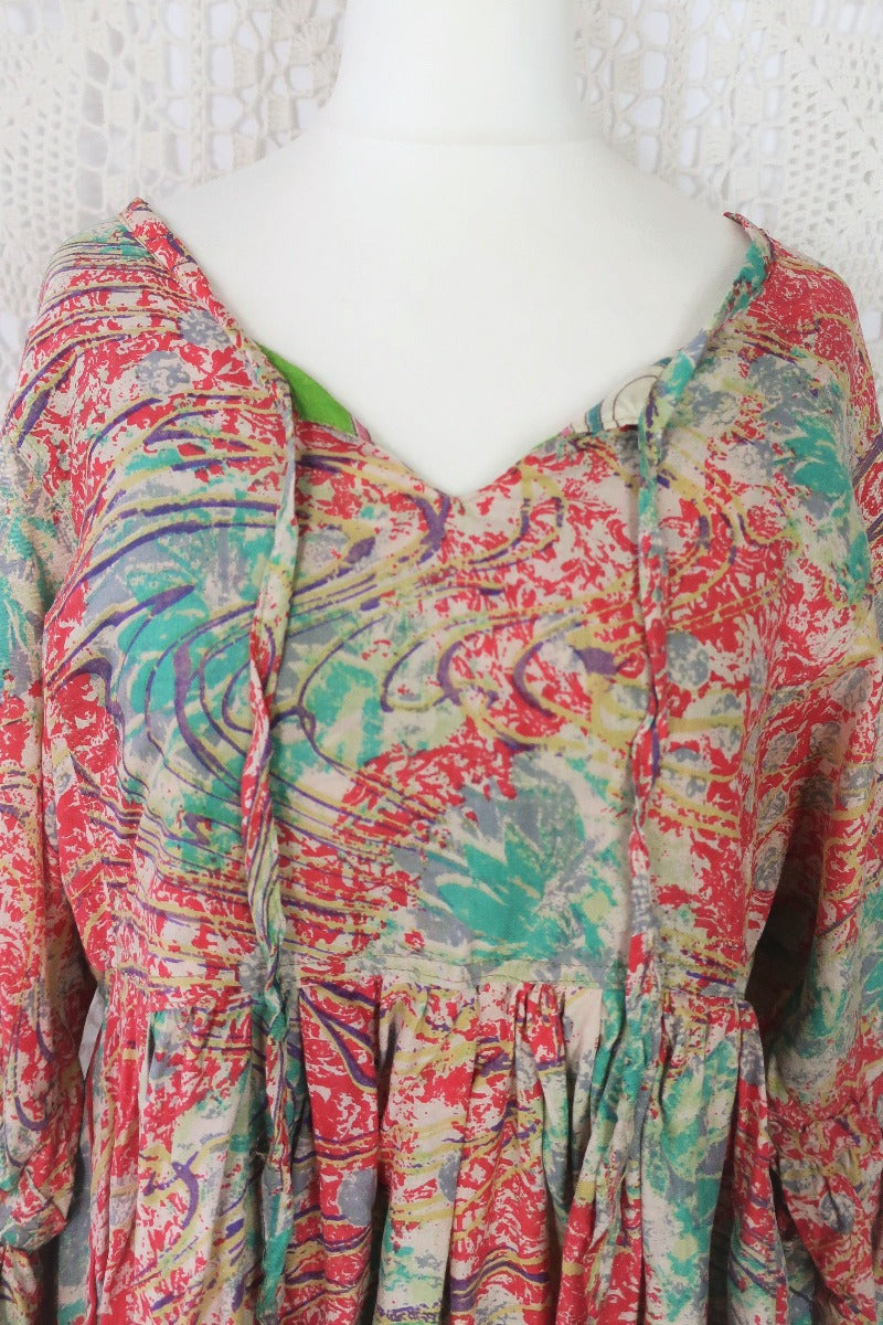Photo shows close up of Daisy smock cotton top in a deep coral pink and aqua colourway and abstract print. Balloon style sleeves and a tie neck top.