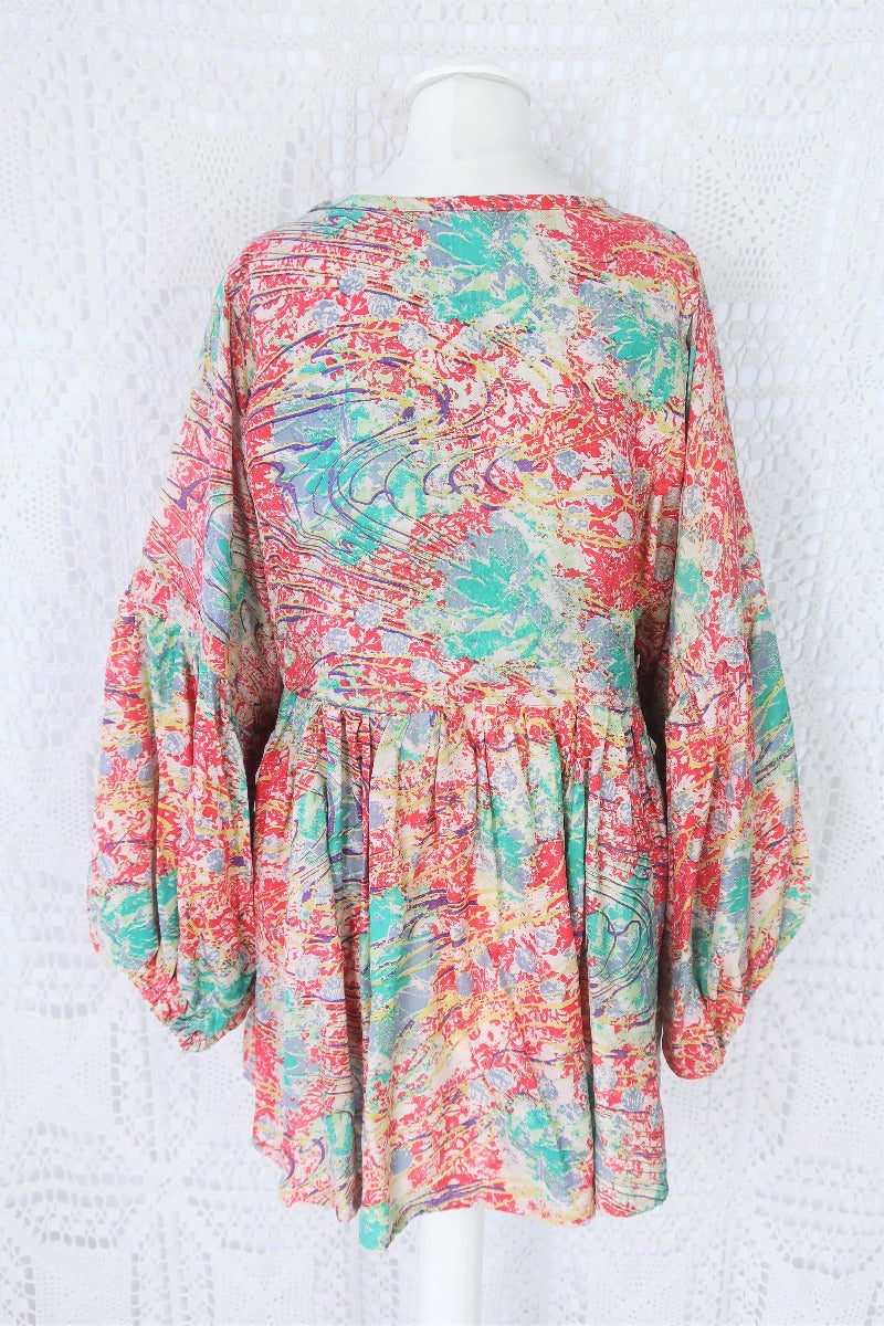 Photo shows back of our Daisy smock cotton top in a deep coral pink and aqua colourway and abstract print. Balloon style sleeves and a tie neck top.