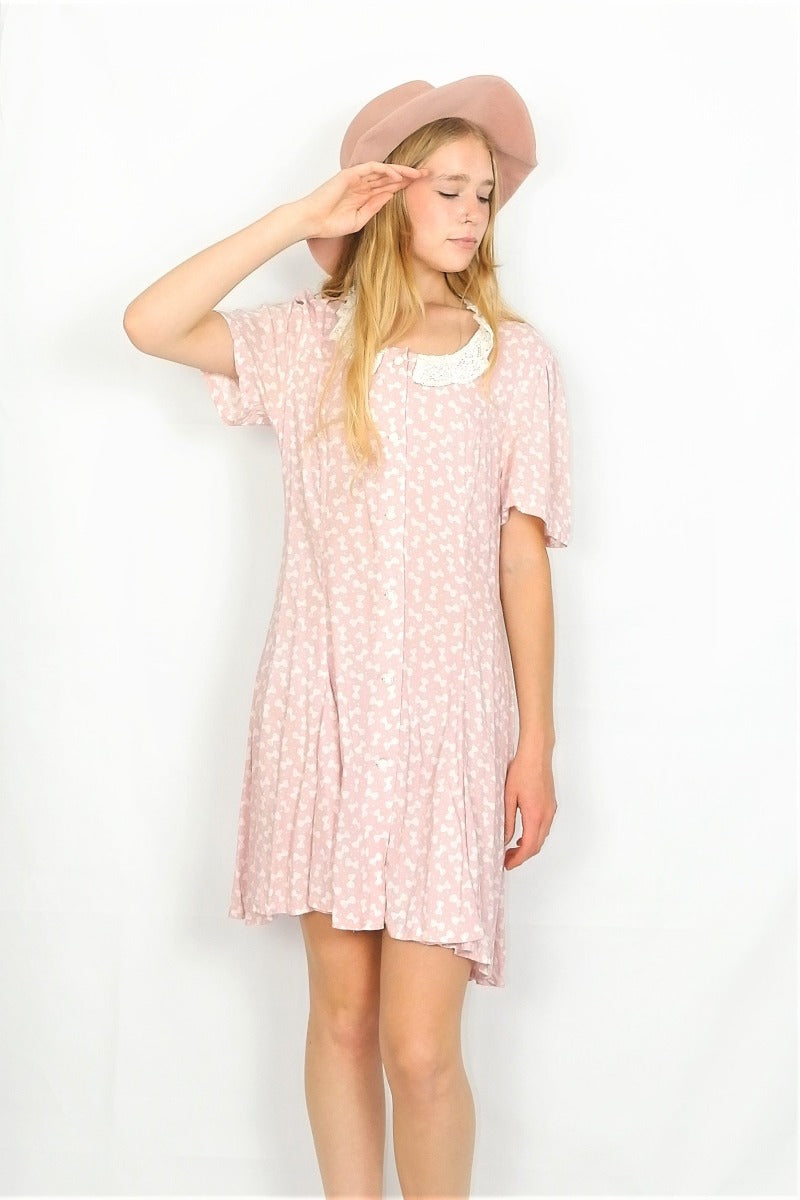 Photo shows full length photo of model wearing a baby pink bowtie polka dot printed mini shift dress with a lace collar.